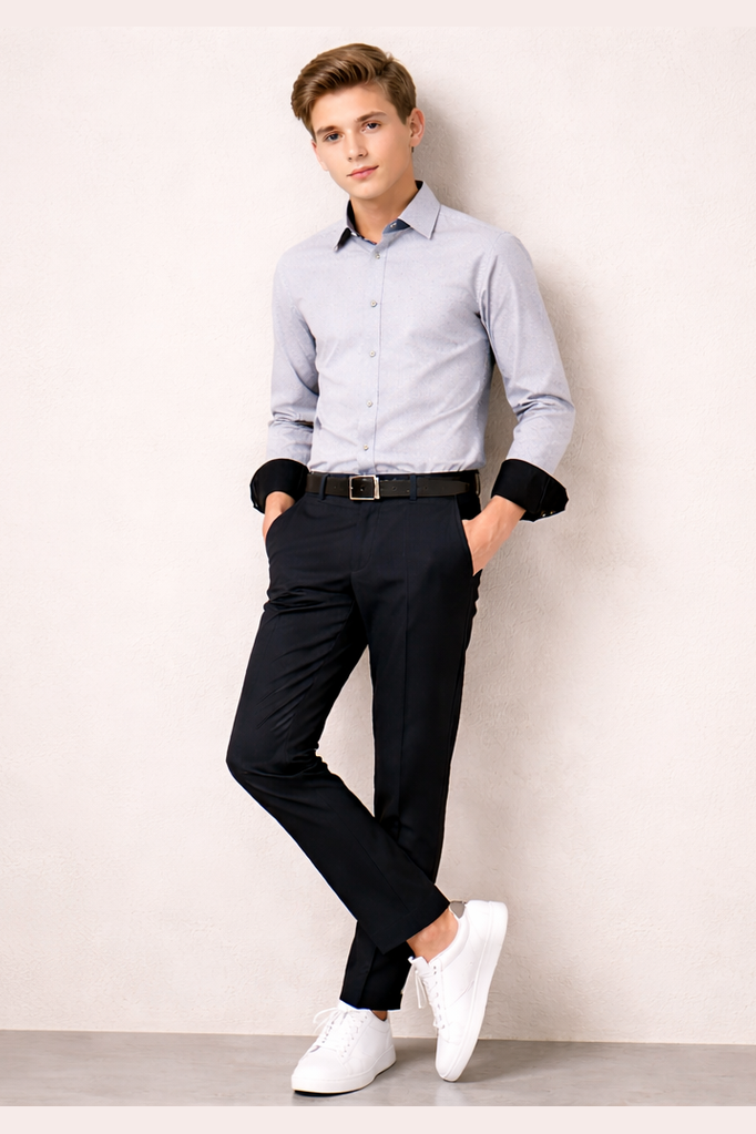 Boy wearing a light blue shirt, black pants, and white shoes against a plain background