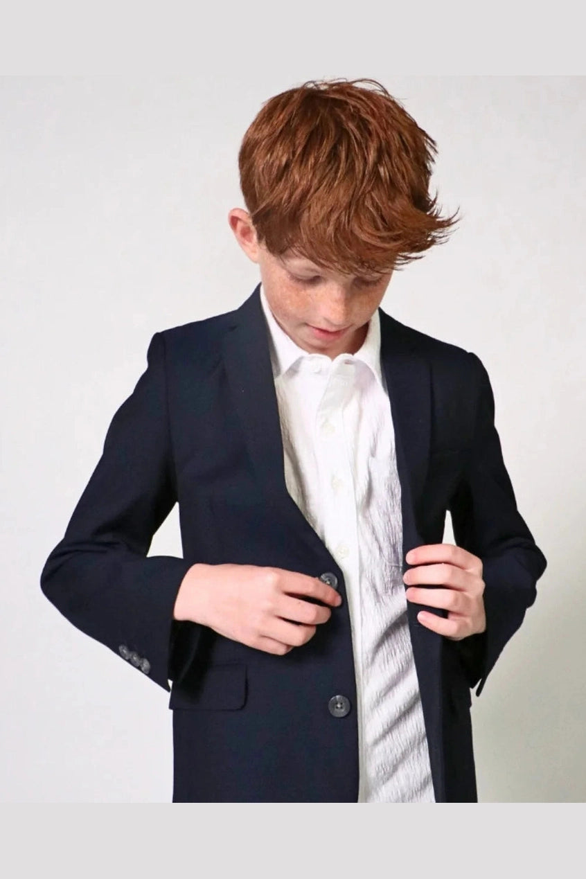 Person wearing a navy blazer over a white shirt with a light-colored background