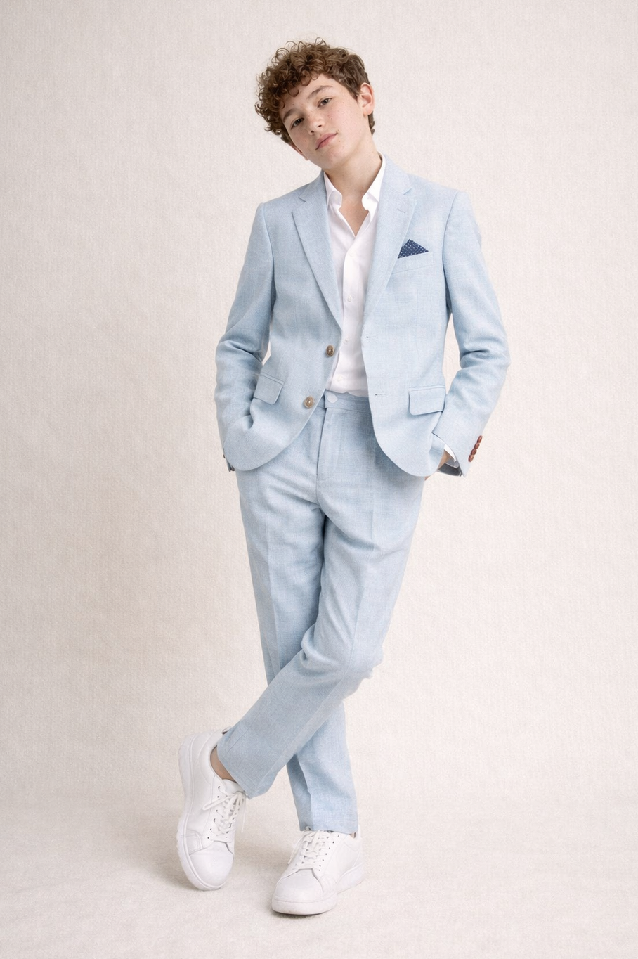 Person wearing a light blue suit with a white shirt and white sneakers on a plain background