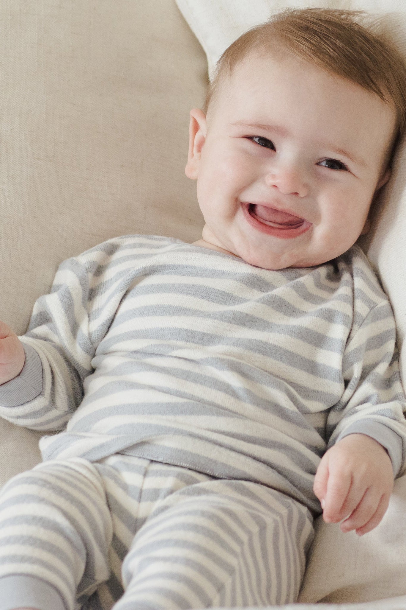 Baby wearing a gray and white striped onesie lying on a beige couch.