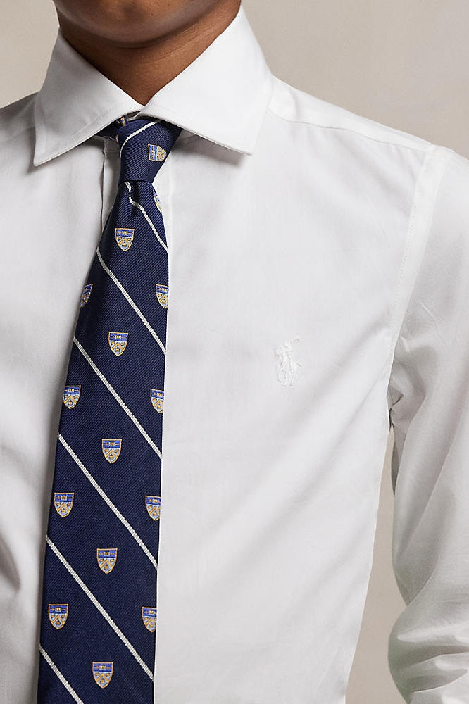 Man wearing a white dress shirt and a navy tie with a pattern, against a neutral background