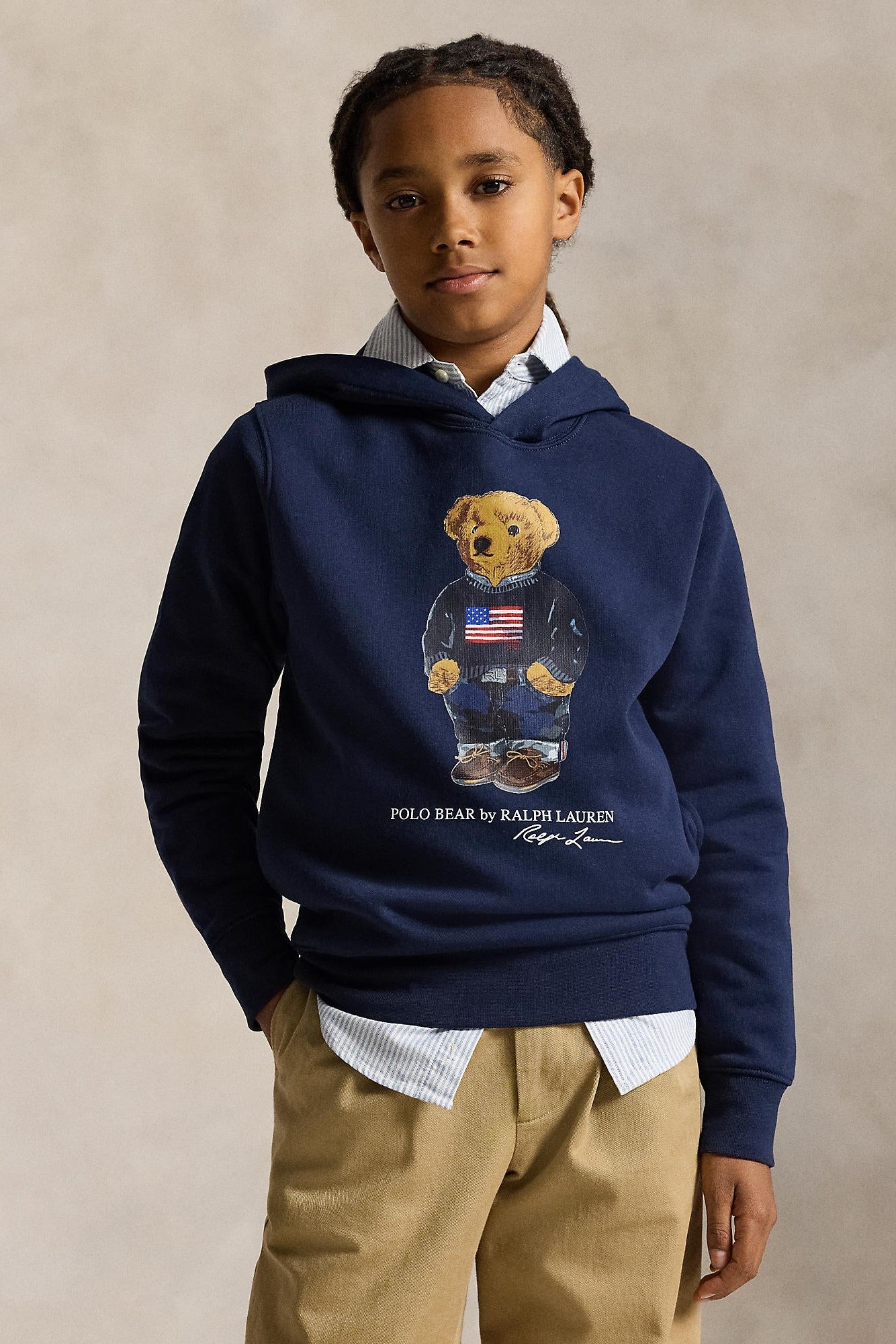 Child wearing a navy hoodie with a bear design and Polo Ralph Lauren logo, standing against a beige background.