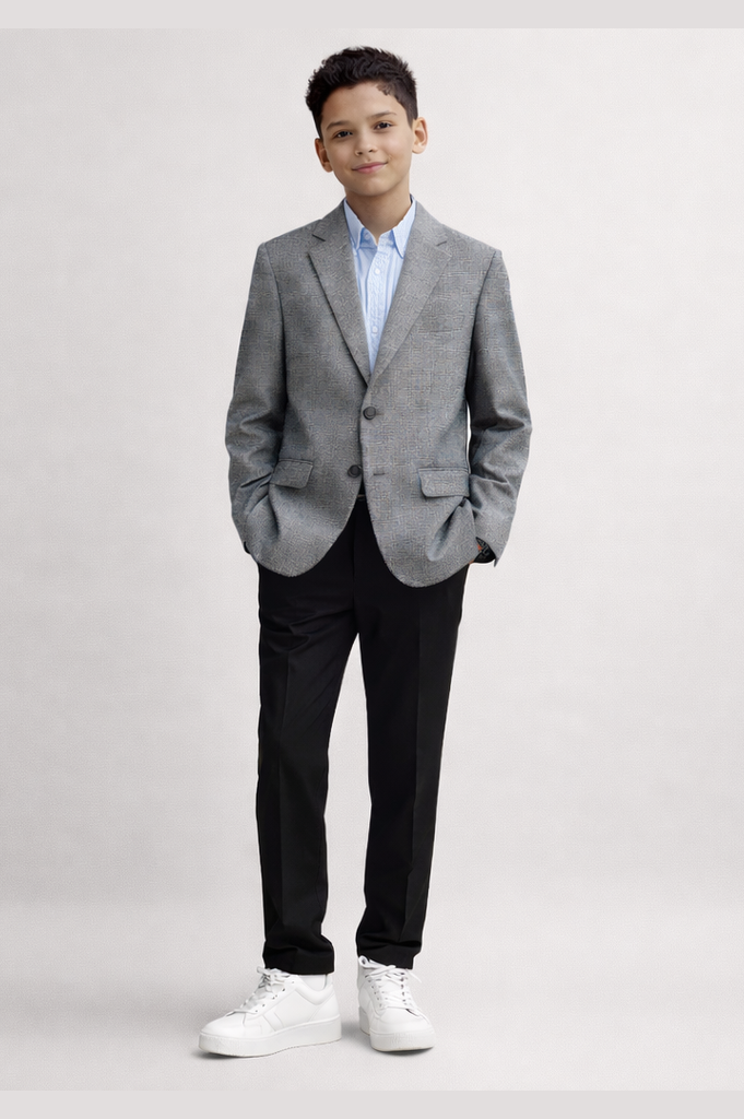 Young boy wearing a gray blazer, black pants, and white shoes on a light gray background