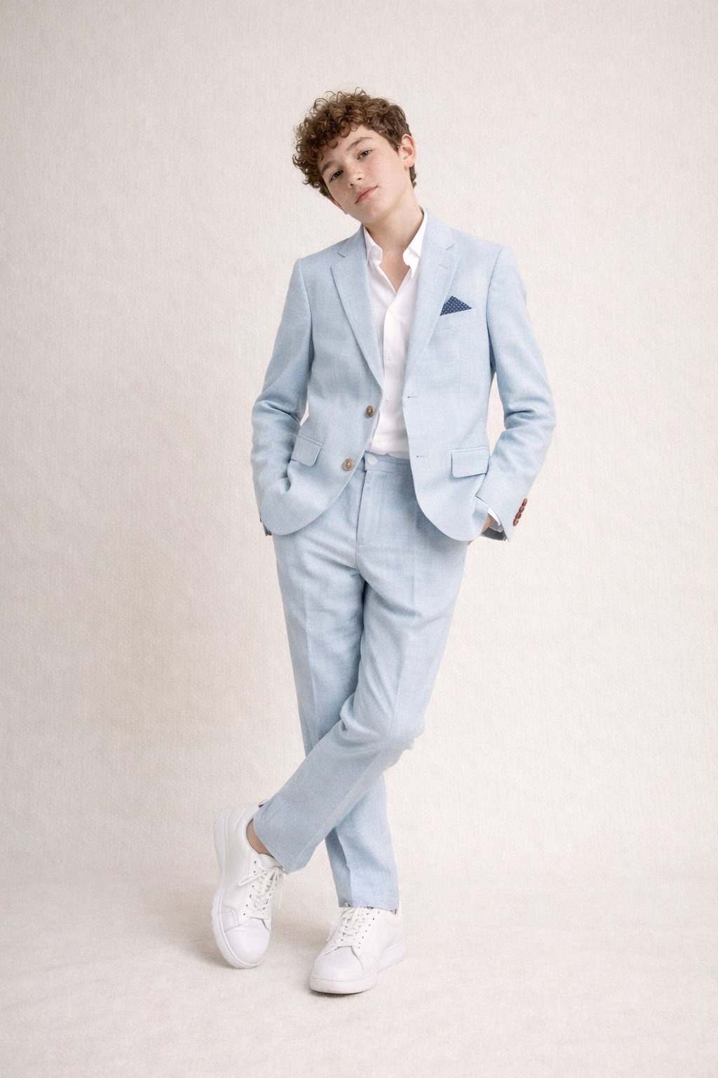 Person wearing a light blue suit with a white shirt and white sneakers on a plain background