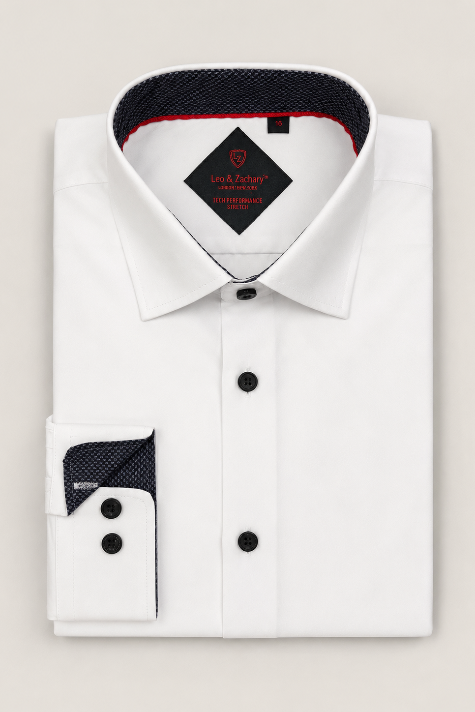 A folded white dress shirt with a pointed collar, black buttons, and a contrasting dark navy patterned inner collar and cuff lining, displayed on a light beige background. The brand label inside the collar reads 'les & factory'.
