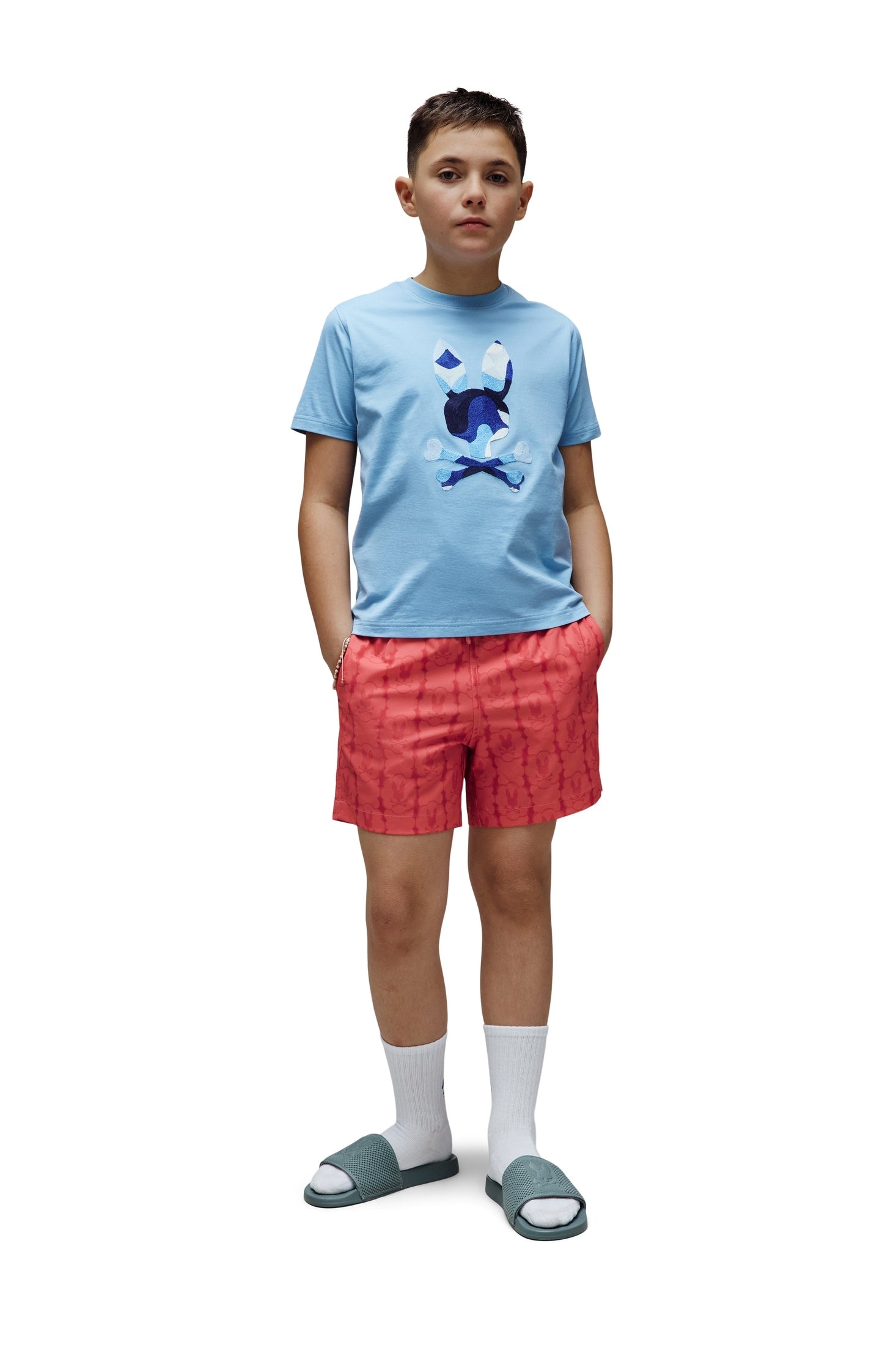 Child wearing a light blue t-shirt with a graphic design and red shorts on a white background