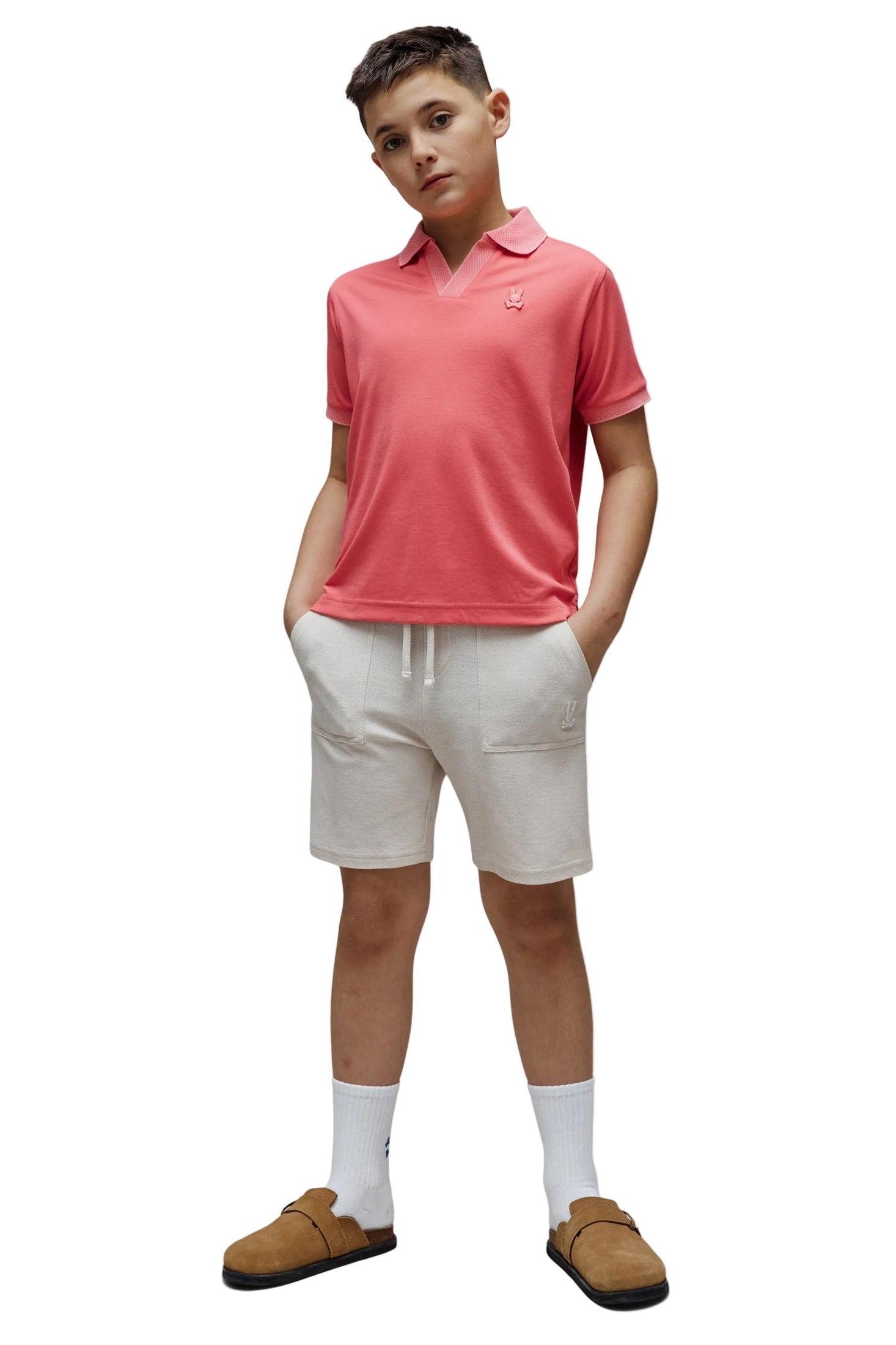 Person wearing a pink polo shirt, white shorts, and brown shoes on a white background