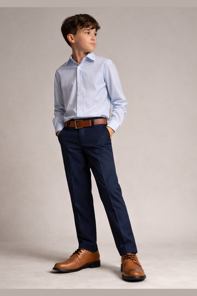 Young boy wearing a light blue dress shirt, navy pants, and brown shoes on a plain background