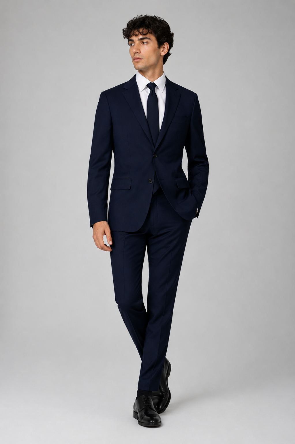 Man wearing a navy suit with a white shirt and black tie on a gray background