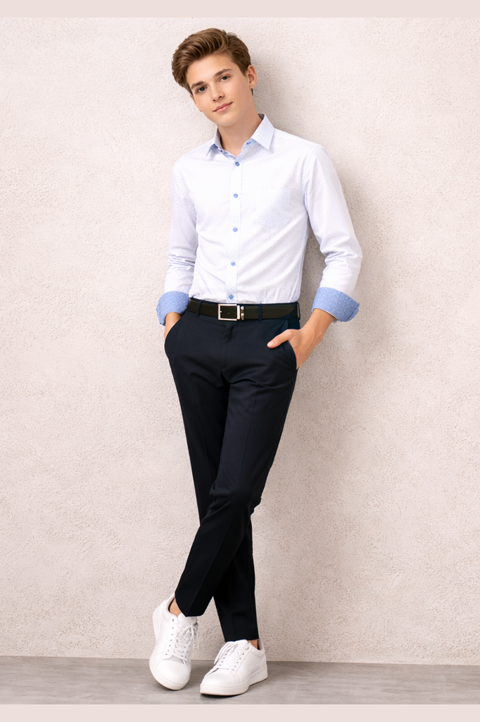 Boy wearing a white dress shirt with rolled-up sleeves, black pants, and white sneakers against a plain wall.